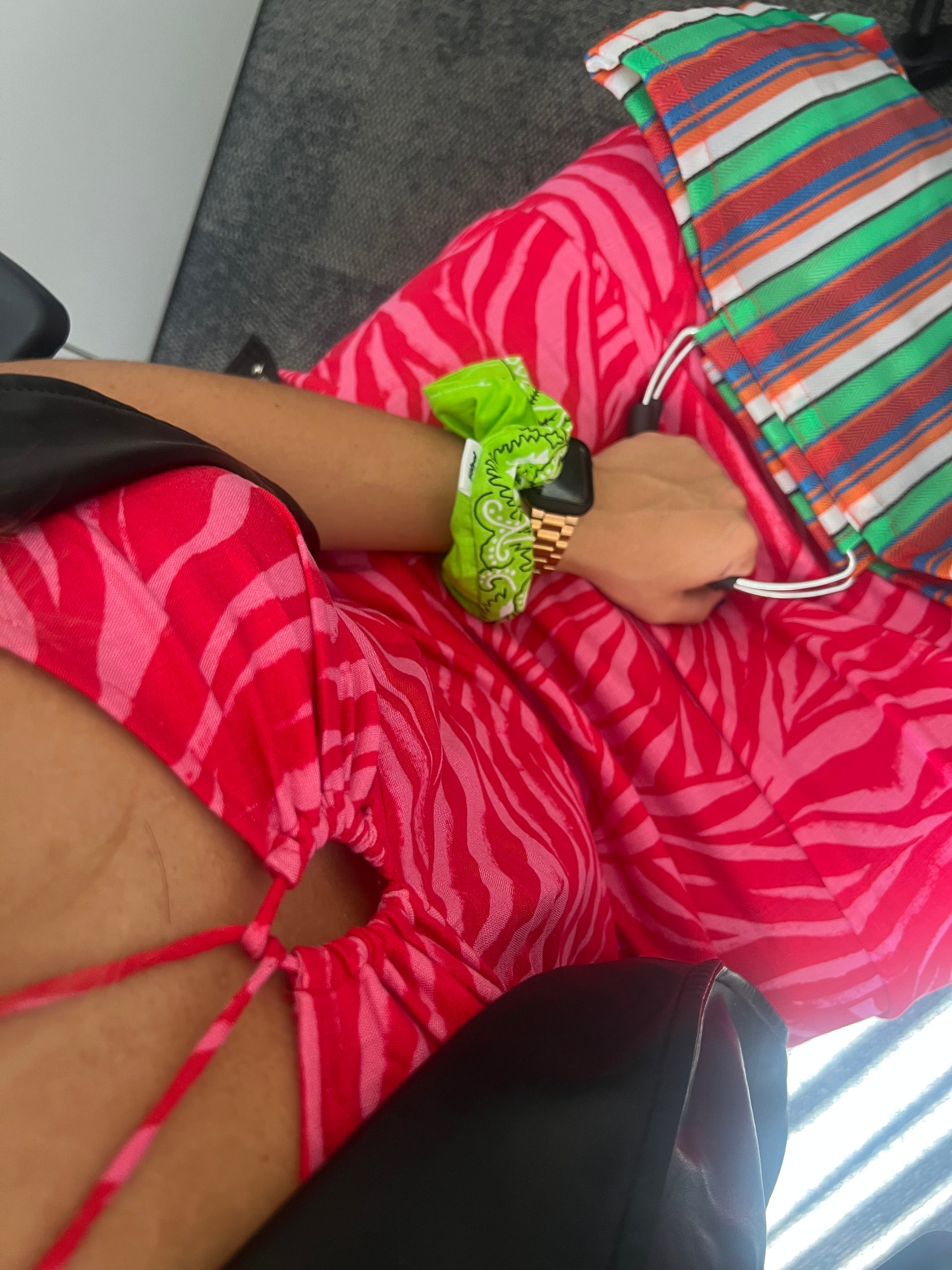 Plano de una chica con un vestido rojo y rosa llevando en la mano el coletero/scrunchie Bandana Acid Green. Sujeta también un bolso de rayas.